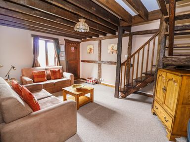 A living room with two beige sofas and a wooden coffee table next to a staircase at Cedar Cottage in Llanidloes