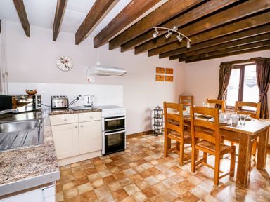 A kitchen with wooden dining table and chairs a stove toaster microwave and sink at Cedar Cottage in Llanidloes