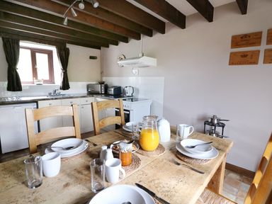 A kitchen with a wooden dining table set for four with plates mugs and a jug of orange juice at Cedar Cottage in Llanidloes