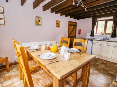 A dining room with a wooden table set for breakfast and kitchen cabinets in the background at Cedar Cottage in Llanidloes
