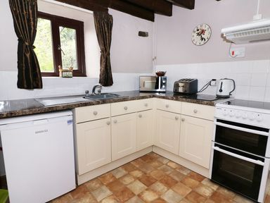 A kitchen with a sink under a window a fridge oven toaster kettle and microwave at Cedar Cottage in Llanidloes