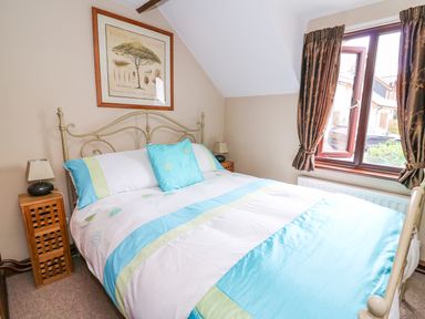 A bedroom with a bed with blue and green bedding a window with brown curtains and a framed picture on the wall at Cedar Cottage in Llanidloes