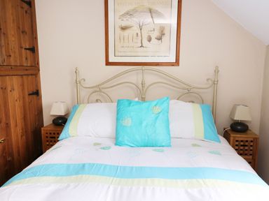 A bedroom with a double bed with blue and white bedding two bedside tables with lamps and a framed picture above the bed at Cedar Cottage in Llanidloes