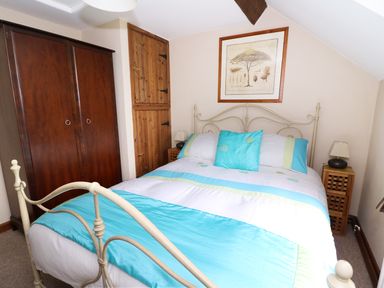 A bedroom with a metal framed bed with blue and white bedding wooden wardrobe bedside tables and framed artwork at Cedar Cottage in Llanidloes