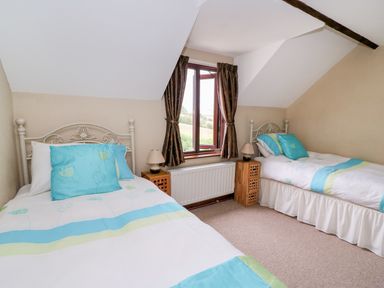 A bedroom with two single beds a window with curtains and bedside tables at Cedar Cottage Llanidloes