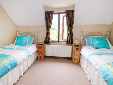 A bedroom with two single beds blue and green bedding wooden bedside tables and a window with brown curtains at Cedar Cottage in Llanidloes