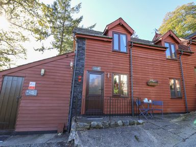 The exterior of a red wooden cottage with a door labeled cedar and two blue chairs with a table outside at Cedar Cottage in Llanidloes