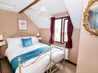 A bedroom with a metal bed frame a window with dark red curtains and a framed picture on the wall at Beech Cottage in Llanidloes