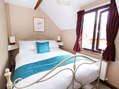 A bedroom with a double bed blue cushions and runner and red curtains at Beech Cottage in Llanidloes
