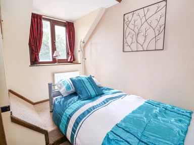 A bedroom with a single bed near a window with red curtains and a decorative wall piece at Beech Cottage in Llanidloes