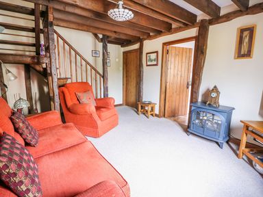 A living room with wooden beams orange sofa and armchair and a blue stove at Beech Cottage in Llanidloes
