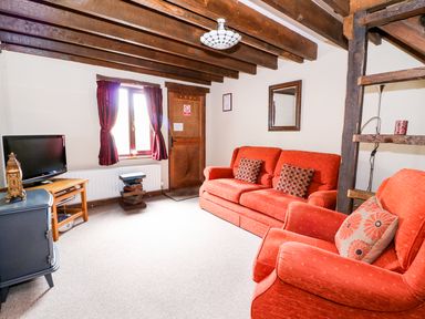 A living room with red sofa and armchair TV and wooden beams on ceiling at Beech Cottage in Llanidloes