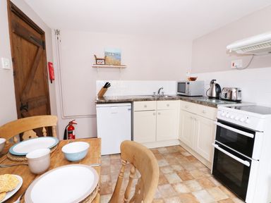 A kitchen with wooden chairs and table set with plates and bowls and white cabinets with appliances at Beech Cottage in Llanidloes