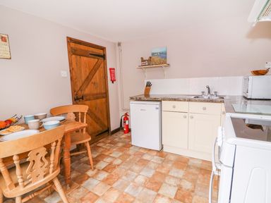 A kitchen with wooden table and chairs a wooden door a small refrigerator sink stove and a microwave at Beech Cottage in Llanidloes