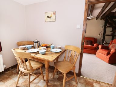 A dining area with a wooden table set for four and an adjacent room with two orange armchairs at Beech Cottage in Llanidloes
