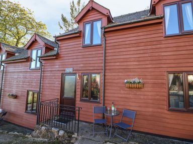 Exterior of a red wooden cottage with windows two chairs and table outside at Beech Cottage in Llanidloes