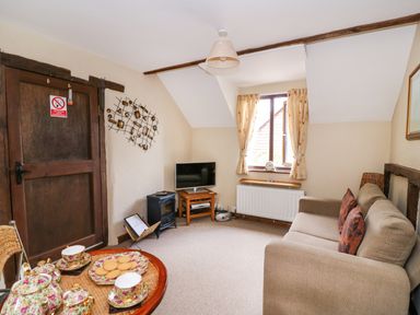 A living room with a sofa a window with curtains a coffee table with tea set and biscuits and a television at Oak Cottage in Llanidloes