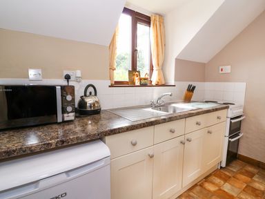 A kitchen counter with a microwave kettle sink knives and stove under a window at Oak Cottage in Llanidloes