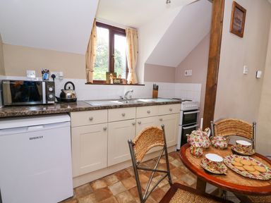 A small kitchen with a microwave, kettle, sink, stove, and a table set with tea cups and biscuits at Oak Cottage in Llanidloes