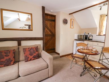 A small room with a beige sofa with two cushions a wooden door a mirror a table set with tea cups and a teapot next to a compact kitchen area at Oak Cottage in Llanidloes