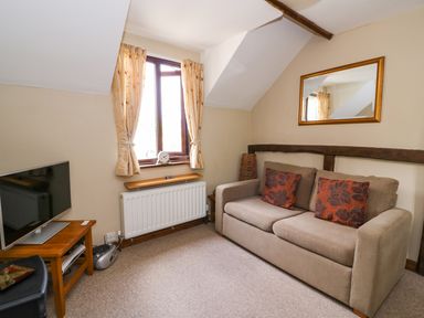 A small living room with a beige sofa with two patterned cushions a wall mirror a window with curtains a radiator a wooden side table with a TV and a stereo unit at Oak Cottage in Llanidloes