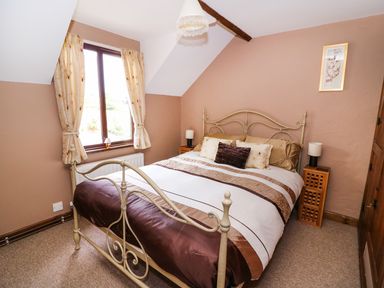 A bedroom with a double bed brown and beige bedding bedside tables with lamps and a window with curtains at Oak Cottage in Llanidloes
