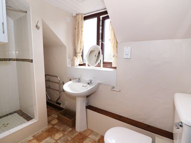 A bathroom with a pedestal sink a shower with tiled walls a window with curtains and a toilet at Oak Cottage in Llanidloes