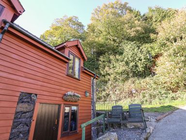 Exterior of a wooden house with a flower box and two chairs near a gravel path at Oak Cottage in Llanidloes