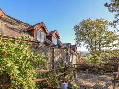 Stone cottage exterior with dormer windows garden pots and tree overlooking countryside at Oak Cottage in Llanidloes