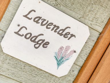 A wooden sign with the text Lavender Lodge and a small painting of lavender flowers on a textured wooden wall at Lavender Lodge in Charlton Horethorne near Sherborne