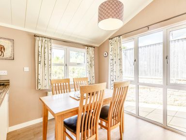 A dining area with a wooden table and four chairs near windows with floral curtains at Lavender Lodge in Charlton Horethorne near Sherborne