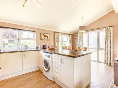 A kitchen with a washing machine under a wooden countertop and a dining area with chairs near windows at Lavender Lodge in Charlton Horethorne near Sherborne