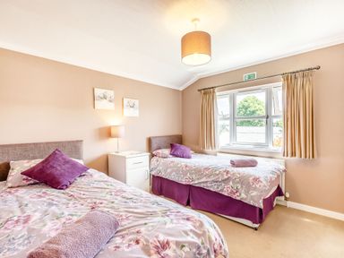 A bedroom with two single beds a nightstand with a lamp and a window with curtains at Lavender Lodge in Charlton Horethorne near Sherborne