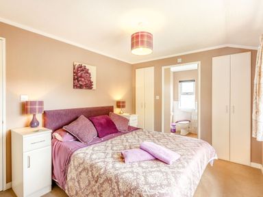 A bedroom with a double bed with patterned bedspread and purple cushions two bedside tables with lamps and an ensuite bathroom at Lavender Lodge in Charlton Horethorne near Sherborne
