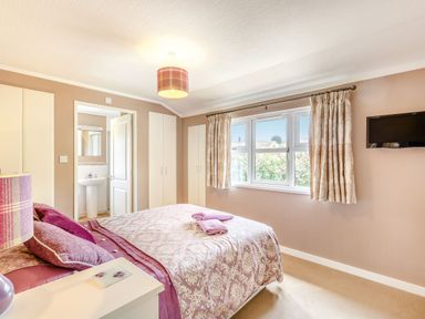 A bedroom with a bed a bedside table a lamp built in wardrobes a window with curtains and a wall mounted television at Lavender Lodge Charlton Horethorne near Sherborne