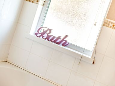 A bathroom window with a purple decorative word Bath on the sill and white tiled walls at Lavender Lodge in Charlton Horethorne near Sherborne