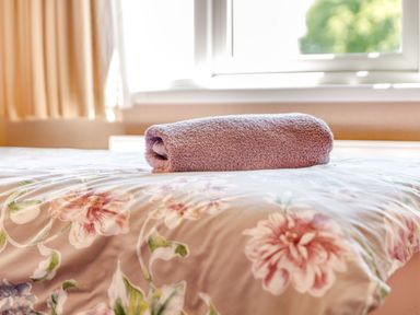 A rolled purple towel on a floral bedspread in a bedroom at Lavender Lodge in Charlton Horethorne near Sherborne