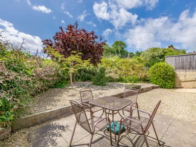 An outdoor patio area with a table and four chairs surrounded by plants and trees at Lavender Lodge in Charlton Horethorne near Sherborne