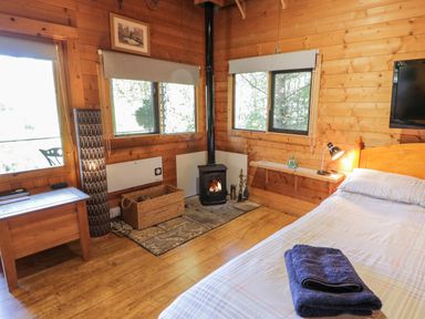 A bedroom with a bed fire stove wicker basket and wooden furniture at The Log Cabin in Oban