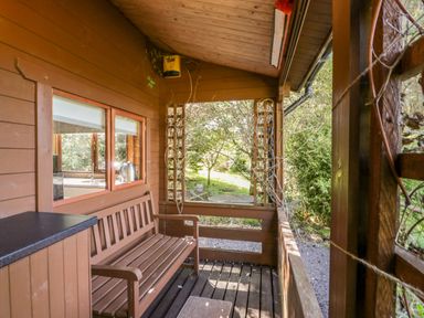 A wooden porch with a bench and lattice panels overlooking a garden at The Log Cabin in Oban