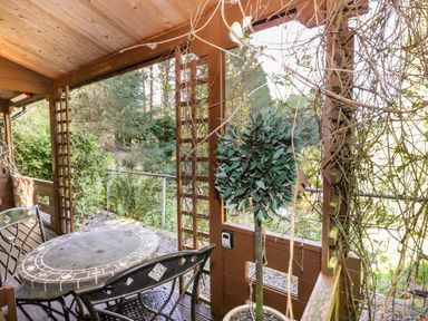 A covered outdoor patio with a round table and metal chairs next to a potted plant at The Log Cabin in Oban