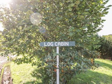 A sign reading log cabin next to green bushes and trees in a grassy area at The Log Cabin in Oban