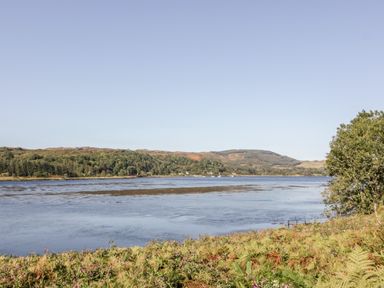 A river with vegetation in the foreground trees and hills in the background at The Log Cabin in Oban