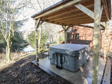 An outdoor hot tub under a wooden pergola near a wooden house by a river at The Log Cabin in Oban