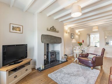 A living room with a television on a stand a wood burning stove a brown leather armchair and a dining table with chairs at 2 Bryn Tirion in Llan Ffestiniog