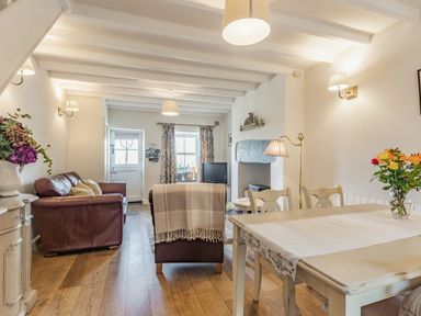 A living room and dining area with wooden floor a dining table with chairs and flowers on the table at 2 Bryn Tirion in Llan Ffestiniog