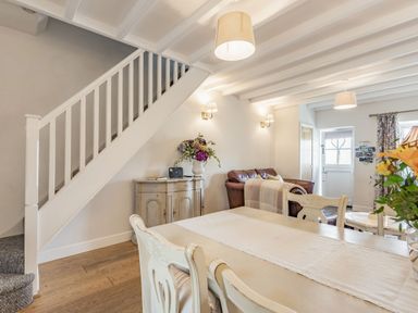 An open dining and living area with a staircase a sideboard with flowers a leather sofa and a door at 2 Bryn Tirion in Llan Ffestiniog