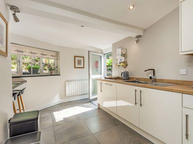 A kitchen with white cabinets a wooden countertop a sink and a door leading outside at 2 Bryn Tirion in Llan Ffestiniog