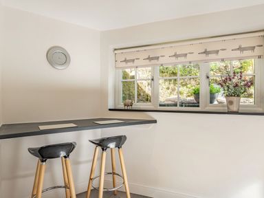 A kitchen nook with two bar stools under a counter and a window with plants at 2 Bryn Tirion in Llan Ffestiniog