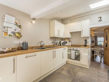A kitchen with white cabinets wooden countertops a sink oven microwave kettle and utensils at 2 Bryn Tirion in Llan Ffestiniog